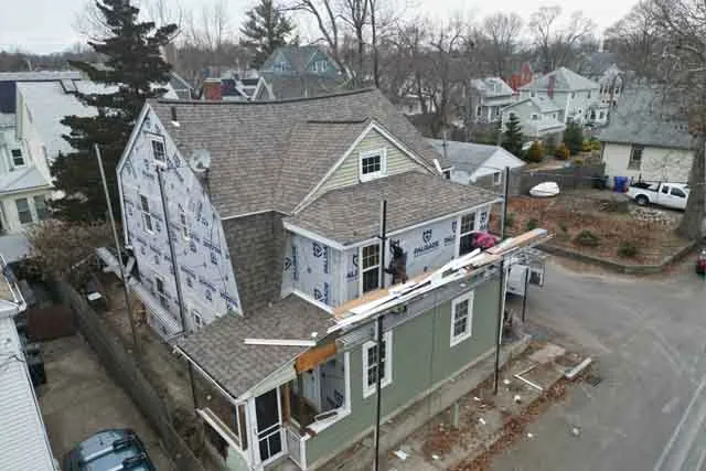 Roofing and siding installation on a residential home in New Bedford, showcasing construction progress with scaffolding and protective sheeting.