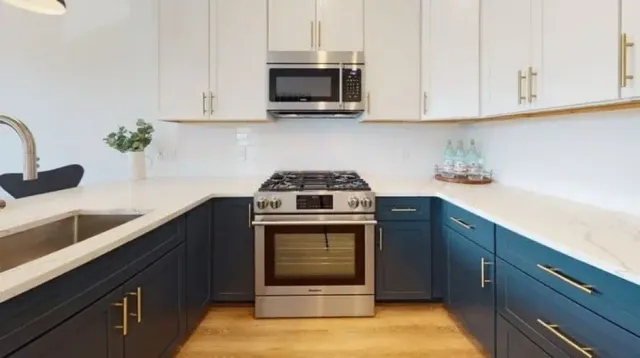 Modern kitchen with navy lower cabinets, white uppers, quartz countertops, and stainless range, located in the Greater Boston area