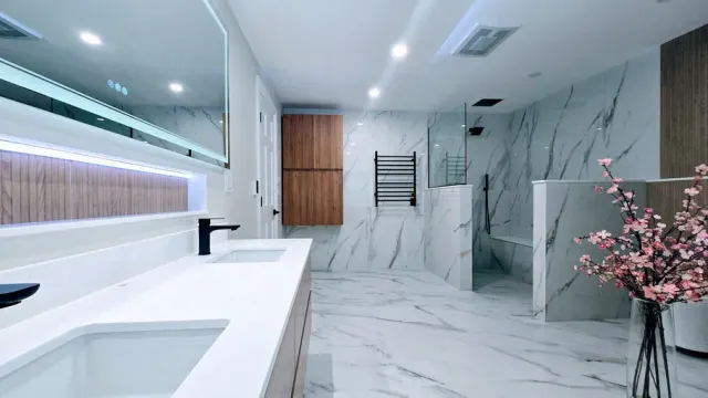 Modern bathroom remodel in Southington, CT with white marble walls, large mirror, double sink vanity, glass shower, and pink flowers.