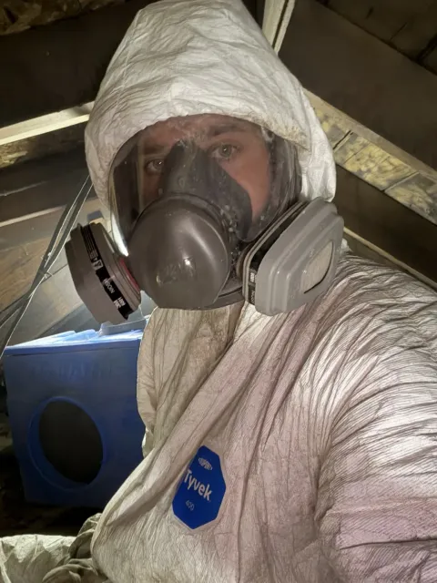 Technician wearing protective coveralls and a full-face respirator inside the attic work area during Smithfield Rhode Island mold remediation project