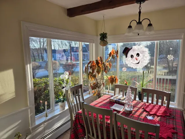 Sunlit dining room with red table runner, wooden table, chairs, and autumn wreath on window overlooking water