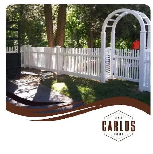 White picket fence with archway in a grassy yard, trees in the background, company logo in bottom corner.