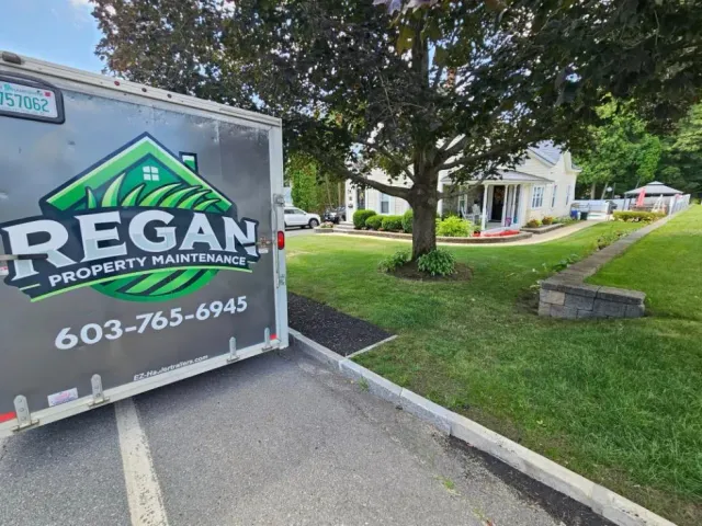 Regan Property Maintenance enclosed trailer parked beside a freshly cut lawn in Hudson, NH