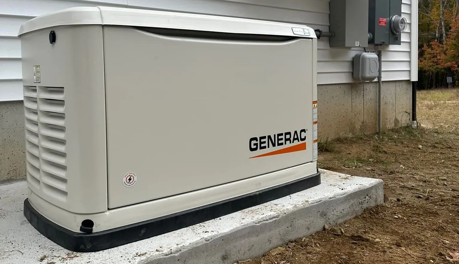 Generator next to a house with gravel border on grass under a cloudy sky.