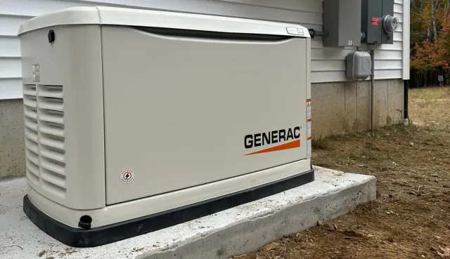 Generator next to a house with gravel border on grass under a cloudy sky.