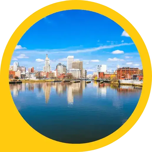A city skyline with tall buildings and historic architecture in Rhode Island, is reflected in a calm river under a bright blue sky with scattered clouds, all framed by a bold yellow border.