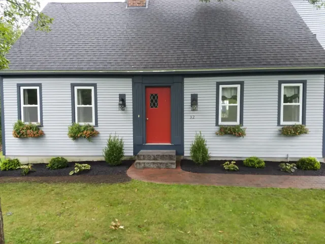 Small gray house with a red front door, white trim, flower boxes, and a green lawn.