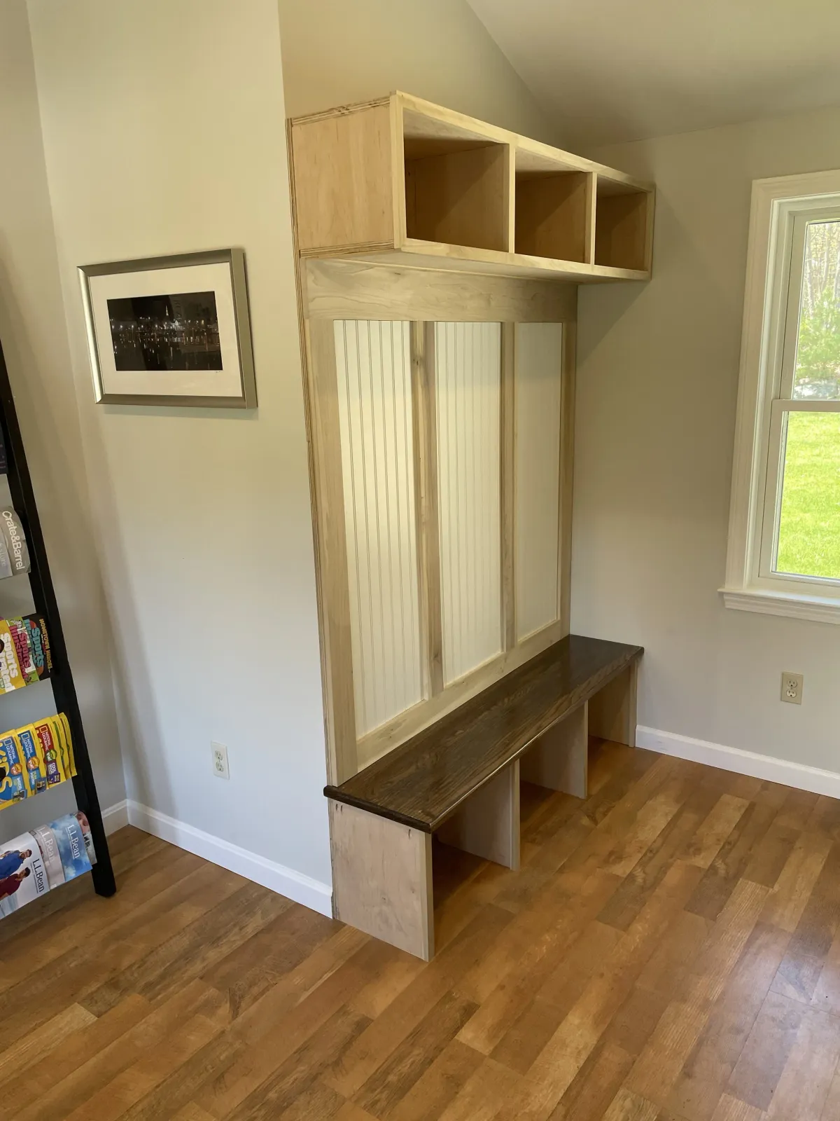 Wooden built-in wall unit with cubbies and a bench in a room with hardwood floors and a window.