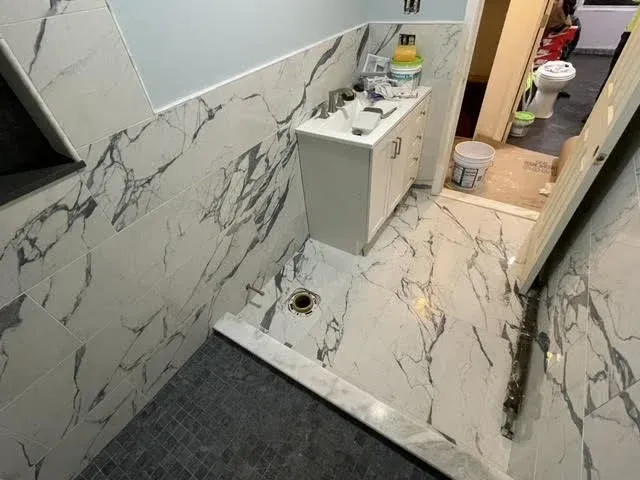 Bathroom with marble tiles on walls and floor, vanity cabinet, plumbing fixtures, and a doorway leading to a toilet area.