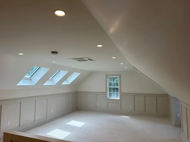 Finished attic renovation in Scituate, MA featuring recessed lighting, skylights, wainscoting, carpet, and hidden storage doors – by New Age Home Improvement LLC.