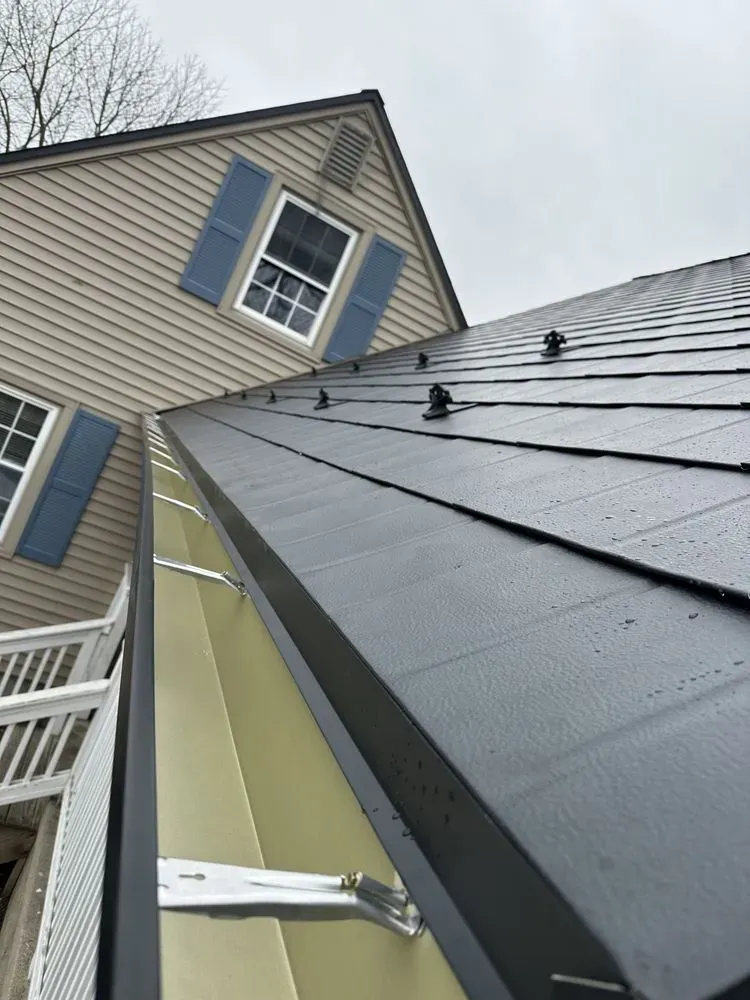 Roof and dormer with blue shutters on a beige house, viewed from below on a cloudy day