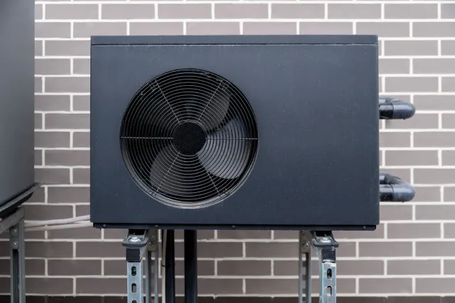 Black rectangular outdoor unit with a large fan on a metal frame against a brick wall