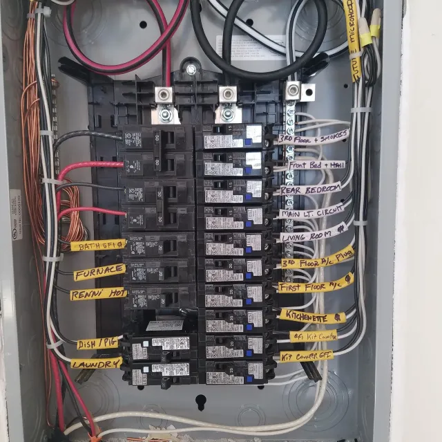 Open electrical breaker panel with labeled circuits and bundled wires.