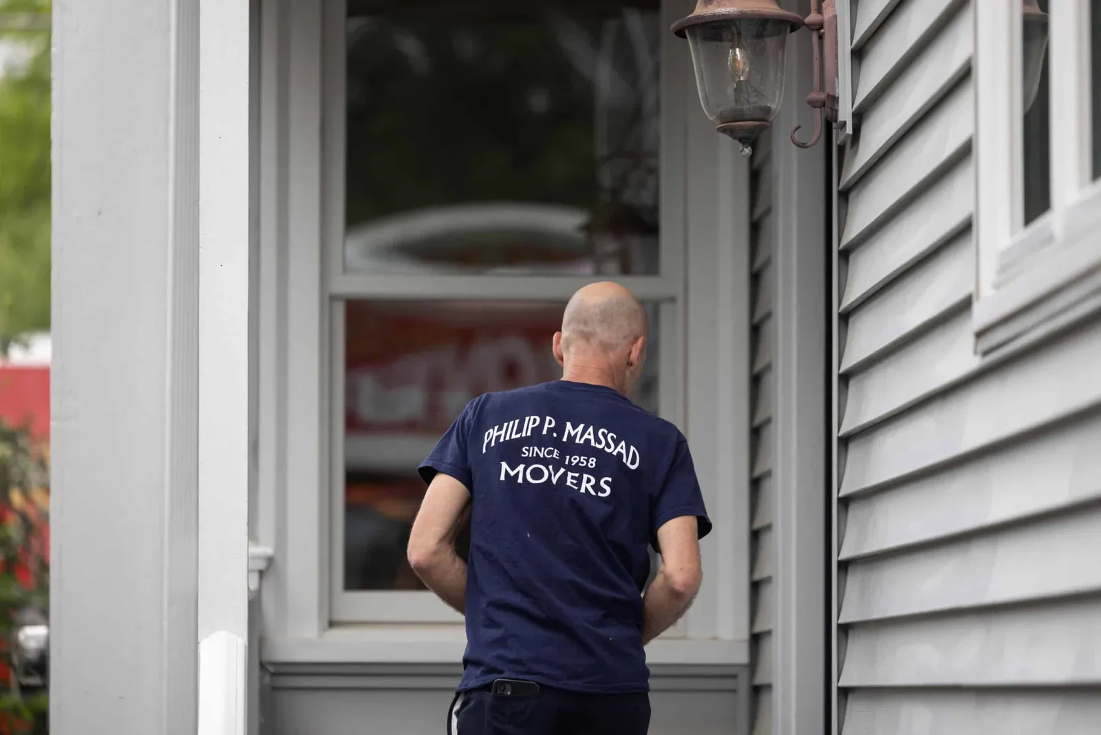 A man in a blue shirt is standing on the porch of a house.