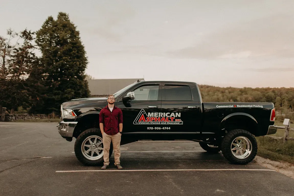A man is standing next to a black truck in a parking lot.