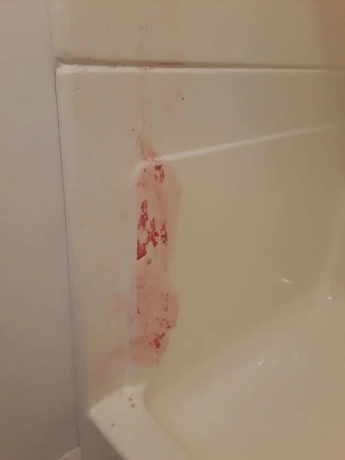Pink stains on a white bathtub wall, likely from a spill or splash.