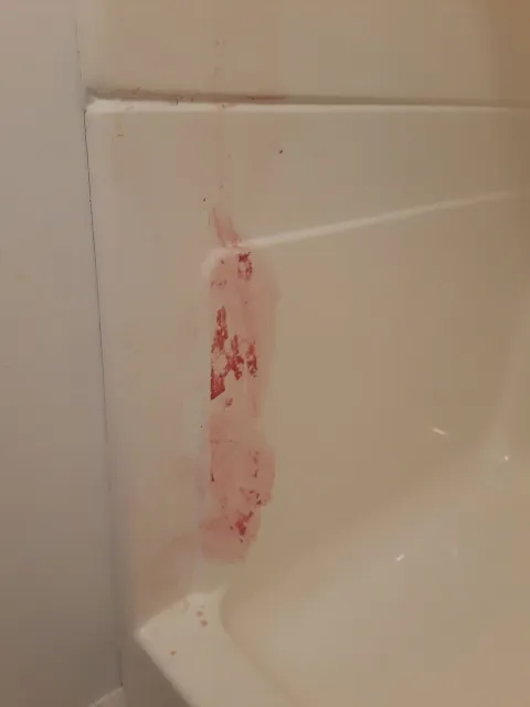 Pink stains on a white bathtub wall, likely from a spill or splash.