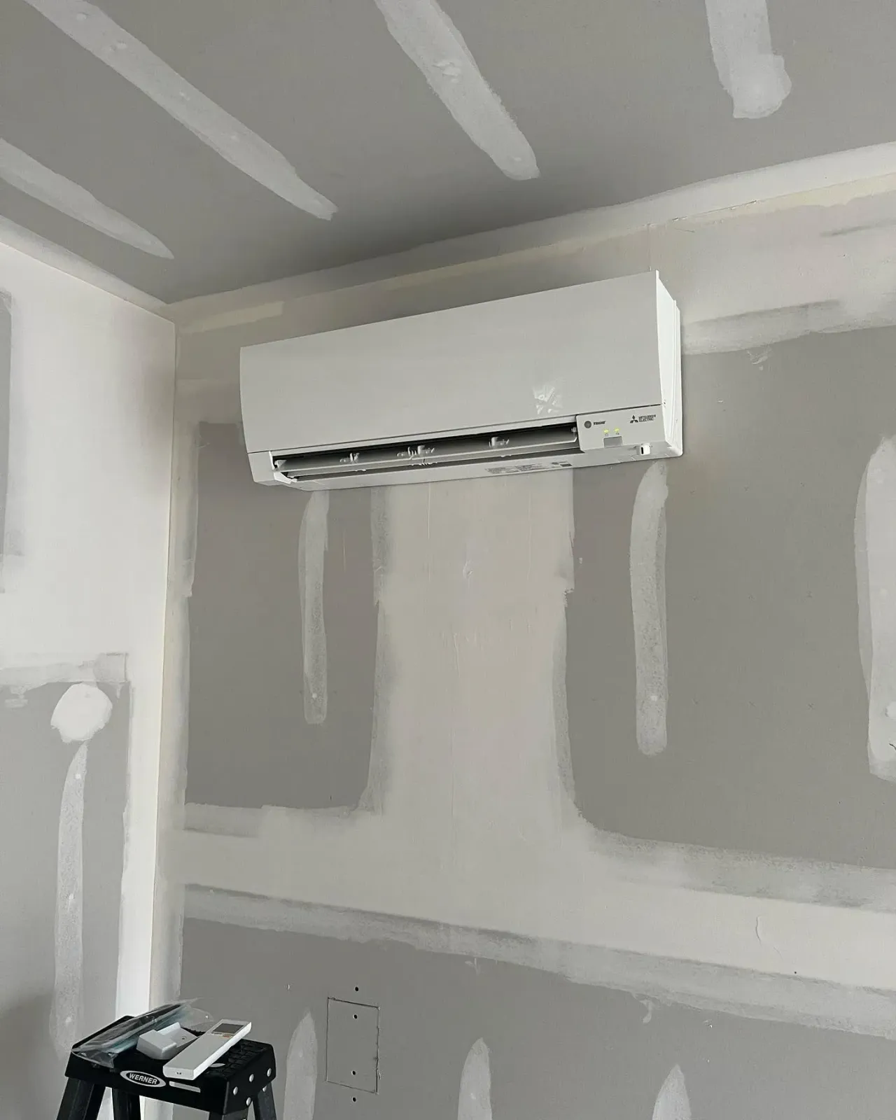 A wall mounted air conditioner is hanging from the ceiling in a room.