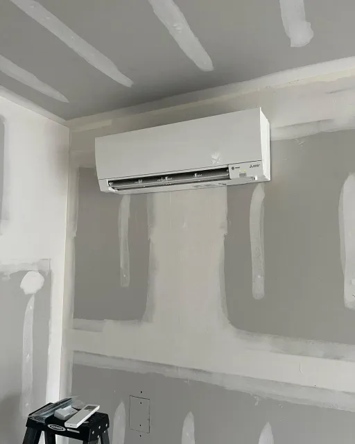 A wall mounted air conditioner is hanging from the ceiling in a room.