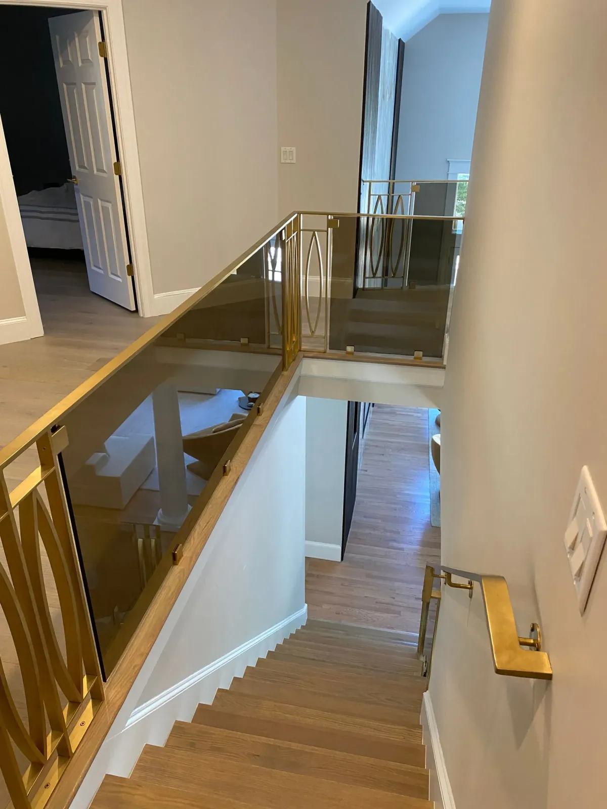 Staircase with wooden steps, gold railing, glass panels, and light gray walls.