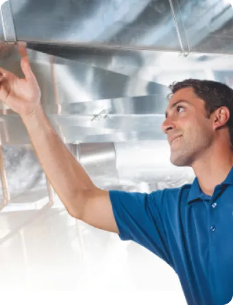 A man in a blue shirt inspects or adjusts a metal air duct