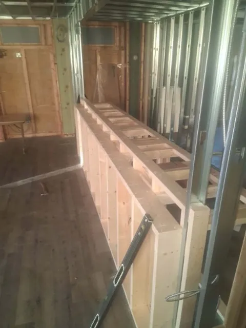 Wood-stud framing for a custom counter and shelving beside a steel-stud wall