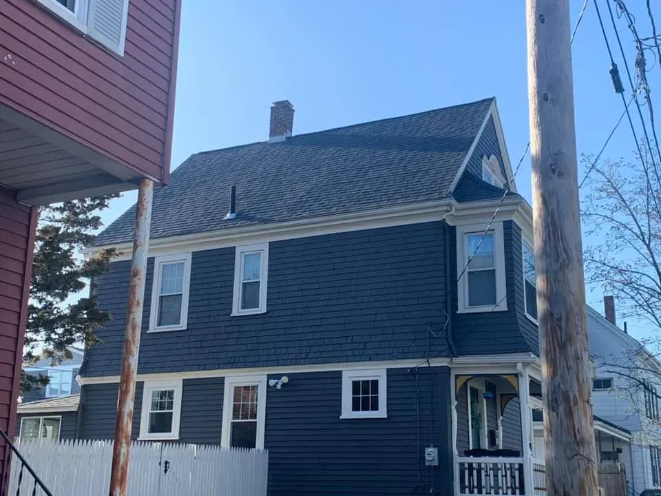 A black house with a white fence and a chimney on the roof.