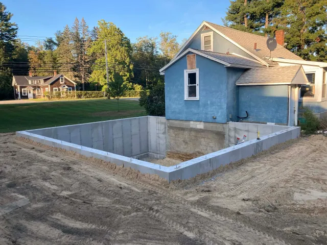 A blue house with a concrete foundation in front of it.