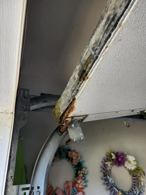 Worn garage door bottom seal and rusted roller before replacement in Randolph, MA