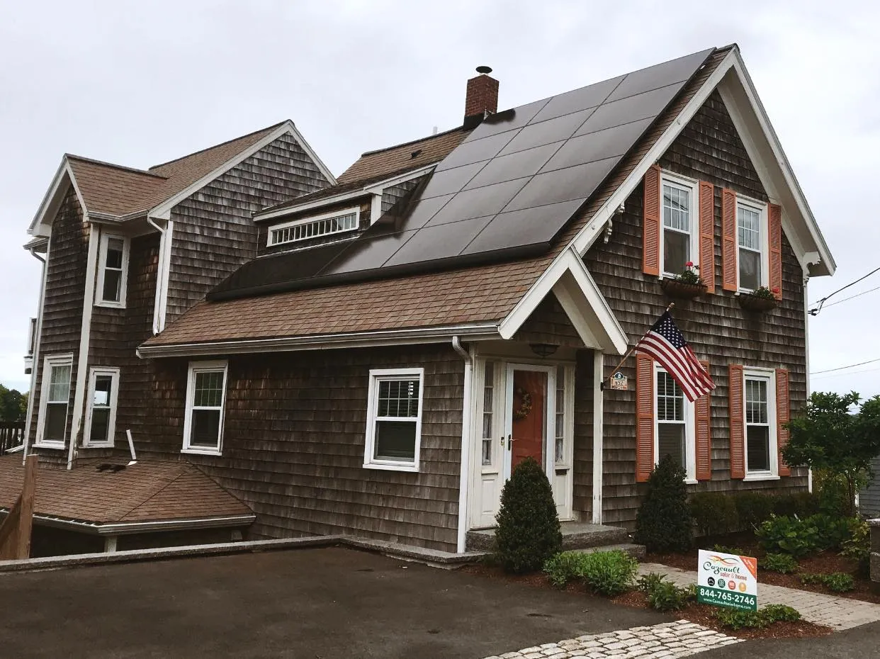 A home in Massachusetts with solar electric (PV) panels on one roof, the house is brown and looks a little older.