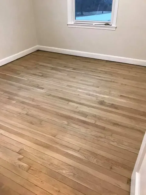 Wooden floor in a room, with a window and white trim.
