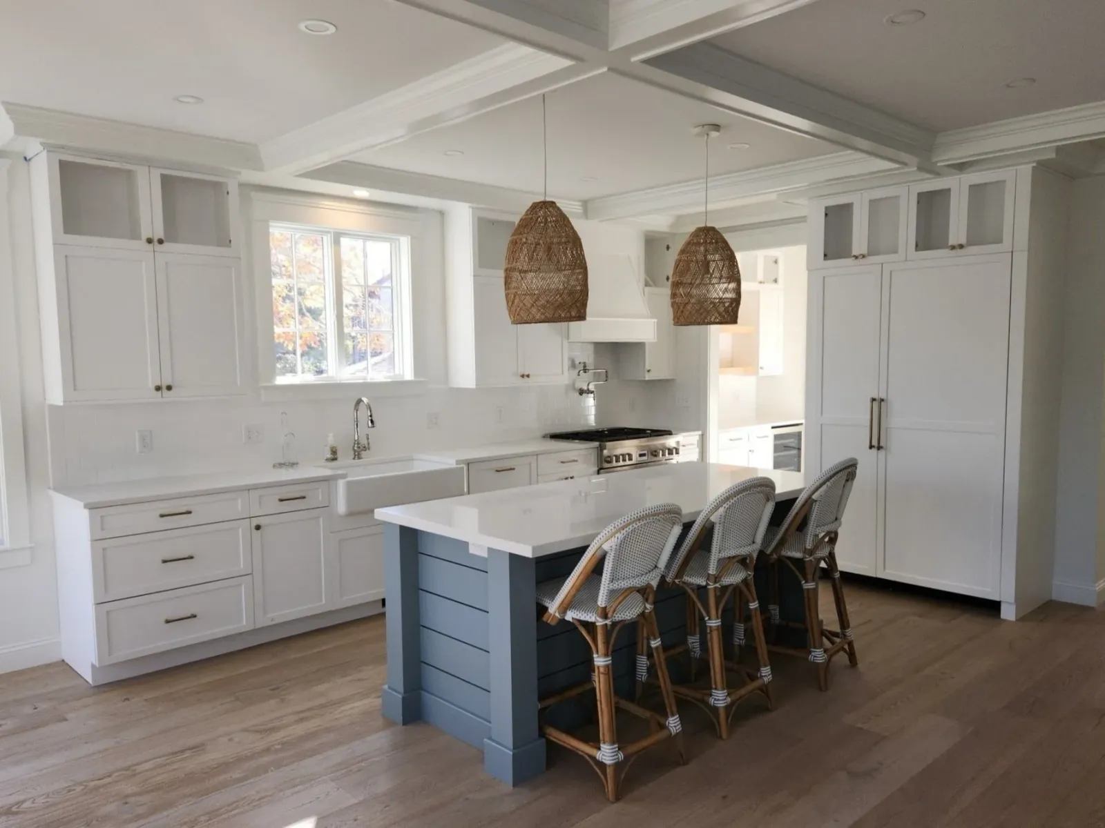 Modern kitchen with white cabinets, large island, wicker pendant lights, and wooden bar stools.