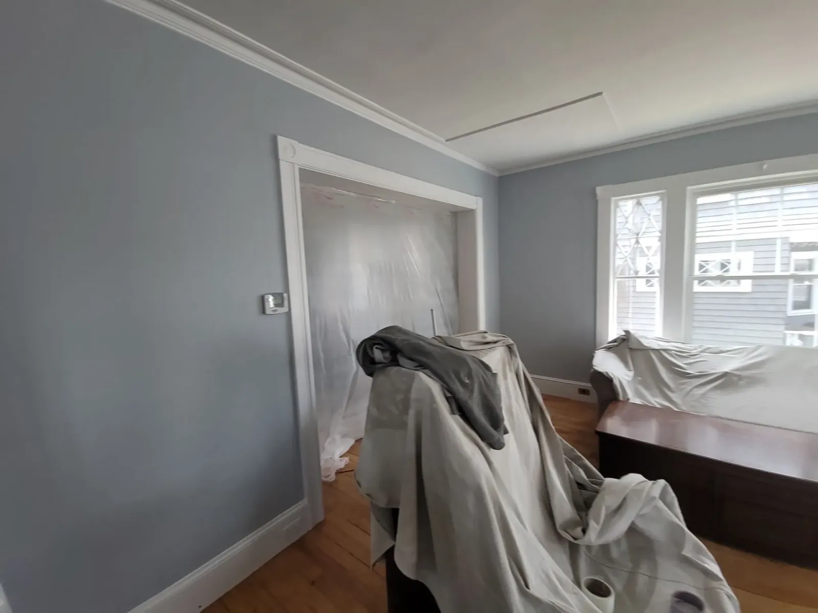 Gray bedroom under renovation with furniture covered in drop cloths and a doorway to another room