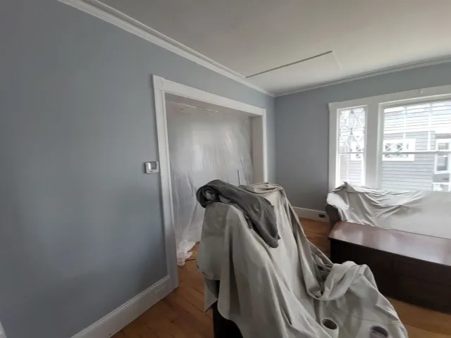 Gray bedroom under renovation with furniture covered in drop cloths and a doorway to another room