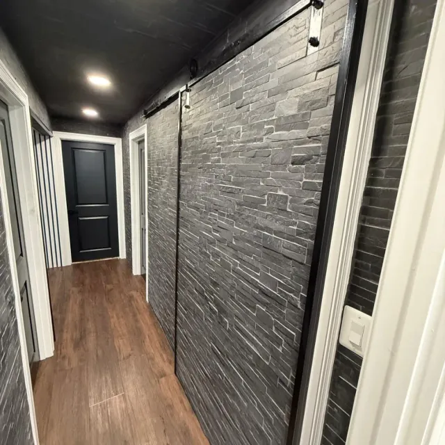 Hallway with stacked stone accent wall, barn-style sliding door and vinyl plank flooring in Arlington, MA — Tinbercraft