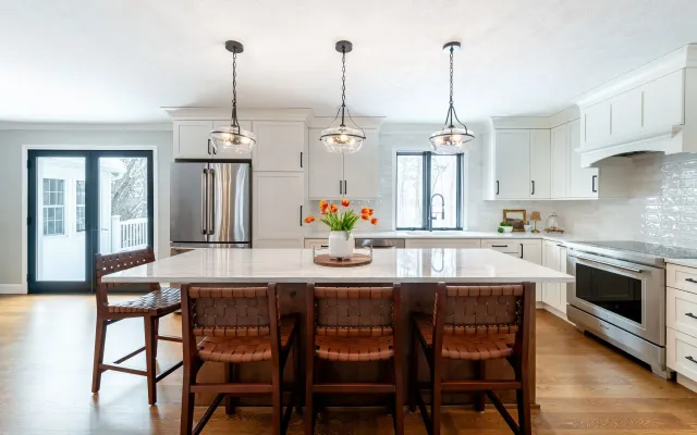 Bright modern kitchen with island, wooden stools, white cabinets, stainless appliances, and pendant lights
