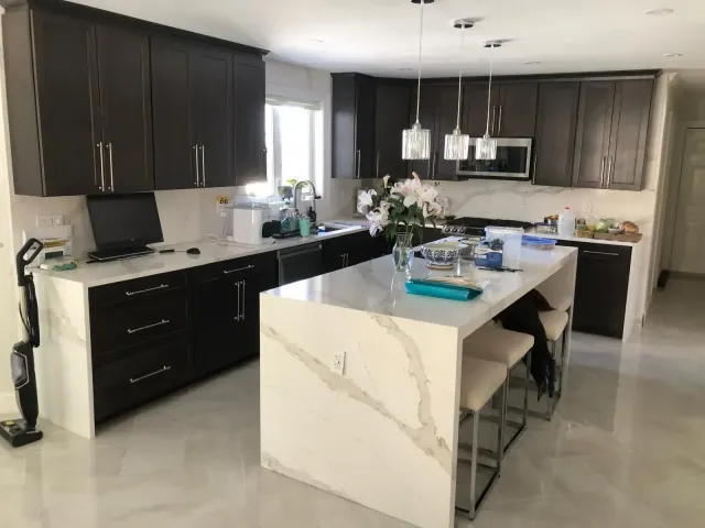 Modern kitchen with dark brown cabinets, white countertops, and island.