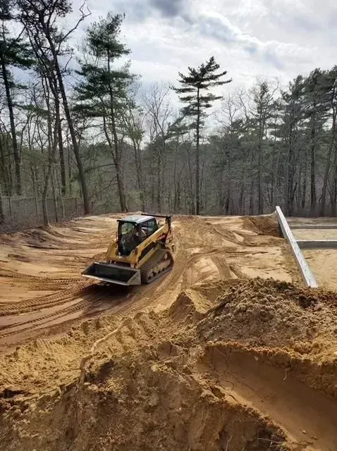Bulldozer grading dirt on a sandy construction site amid bare trees and cloudy sky