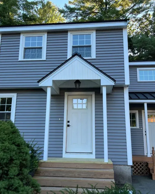 White entry door with divided-lite glass under a new gabled portico on grey vinyl siding, by Maia Construction