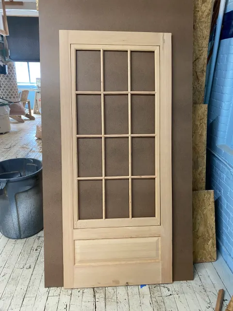 unfinished wooden door with glass panes leaning against a brown wall in a workshop.