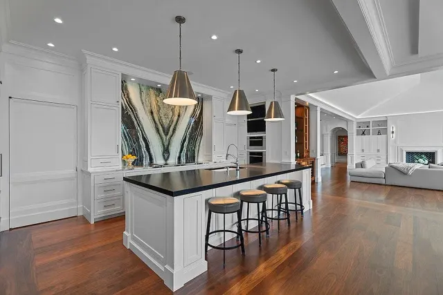 Elegant kitchen with dark wood floors, white cabinetry, island with stools, and abstract art backsplash.