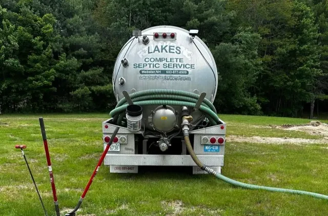 Septic service truck, silver tank, green hose, parked in a grassy yard.