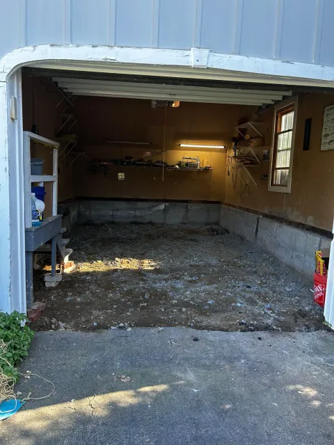 Open garage with a dirt floor, tools, and a window.