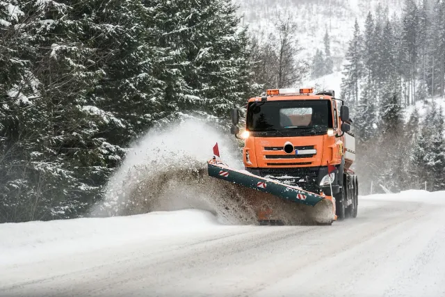 An orange snow plow is plowing snow on a snowy road.