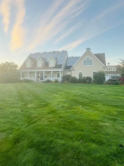 Large beige house with a gray roof and a wide green lawn under a bright sunset sky