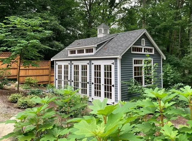 A small house with a lot of windows and doors is surrounded by trees.