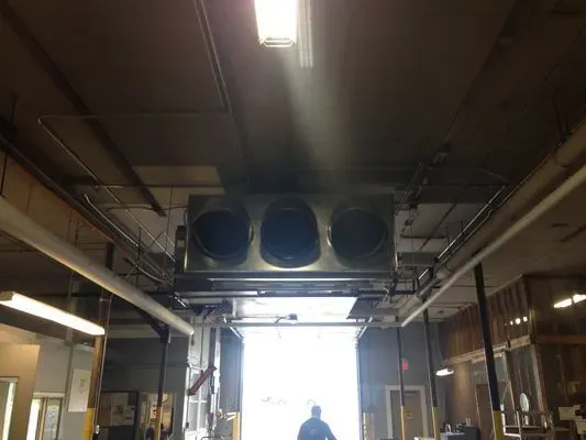 A large, three-nozzle air ventilation unit suspended from a commercial ceiling above an open warehouse loading bay.