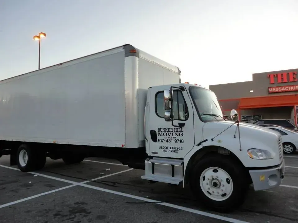A white moving truck parked in a lot in front of a building with an orange sign.