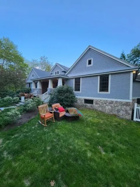 Gray house with a stone foundation and two lounge chairs on a green lawn under a blue sky