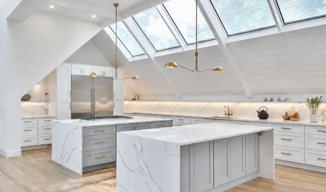 Modern white kitchen with marble countertops, large island, skylights, and custom cabinetry